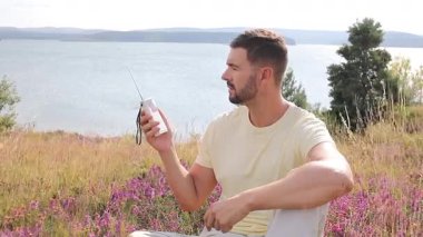 Genç adam gölün kenarında oturuyor ve radyoyu tutuyor.