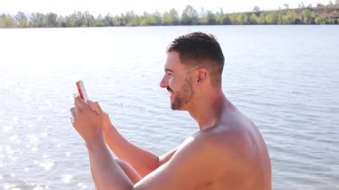 Gölün arka planında akıllı telefonlu yakışıklı bir genç adam.