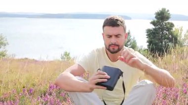 Adam göl kenarında siyah dürbünle dışarıda oturuyor.