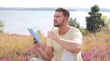 Yellow Shirt giyen, defterli, açık havada suya yakın bir adam.