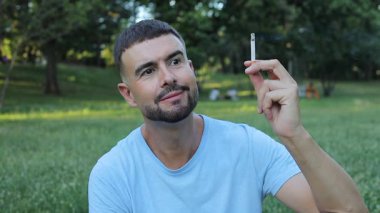 Genç adam parkta sigara içiyor.