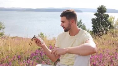 Yakışıklı adam gölün kenarında oturuyor ve radyoyu tutuyor.