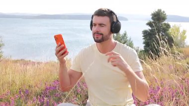 Kulaklıklı yakışıklı adam doğada akıllı telefonla müzik dinliyor.