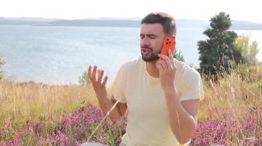 Göl kenarındaki akıllı telefona konuşan kızgın adam.
