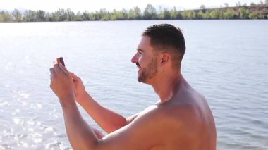gölün arka planında akıllı telefonlu yakışıklı bir genç.