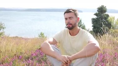 Genç adam, gölün kenarında elinde çiçeklerle sigara içiyor.