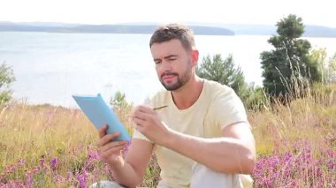 Mutlu adam göl kenarında deftere yazıyor.