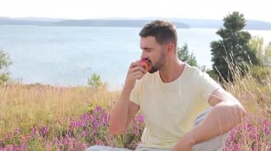 Mutlu genç adam doğada elma yiyor.