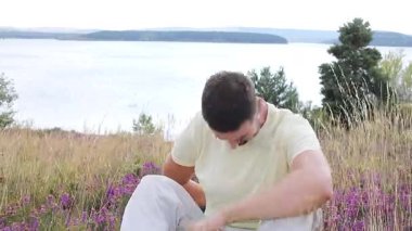 Pembe güllü genç adam Gölün yanındaki tepede oturuyor. 