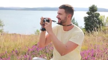 Gölün ve çiçeklerin arka planında kamerası olan yakışıklı bir fotoğrafçı.