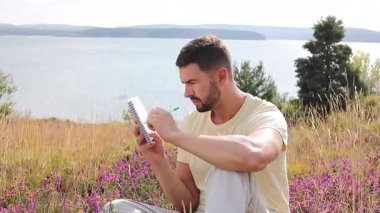 Göl kenarındaki defterde yazan yakışıklı adam.