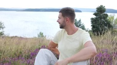 Pembe güllü genç adam Gölün yanındaki tepede oturuyor. 