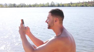 gölün arka planında akıllı telefonlu yakışıklı bir genç.
