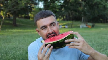 Yeşil çimlerde karpuz yiyen yakışıklı adam.