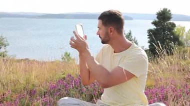 Gölün ve çiçeklerin arka planında ayna olan genç bir adam.