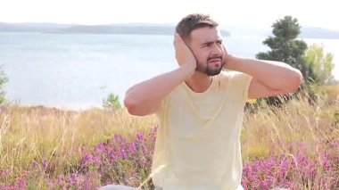 Adam su kenarında otururken Gürültüden ya da stresten Elleriyle Kulaklarını Kapıyor.