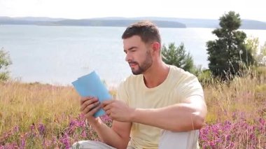 Yazın göl kenarında kitap okuyan yakışıklı bir adam.