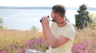 Adam dışarıda oturuyor, elinde bir çift siyah dürbün tutuyor.