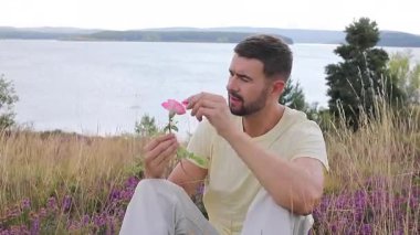 Pembe çiçekli genç adam Gölün yanındaki tepede oturuyor. 