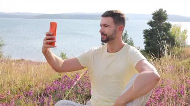 Güneşli bir günde gölün kenarında selfie çeken yakışıklı bir adam.