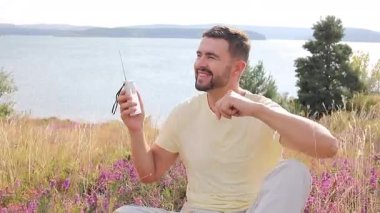 Bir gölün yamacında radyoyla oturan yakışıklı bir adam.