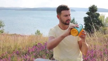 Termoslu genç bir adam Çiçekli çayır ve göllü bir çay