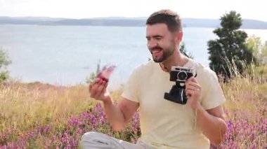 Gölün ve çiçeklerin arka planında kamerası olan yakışıklı bir fotoğrafçı.