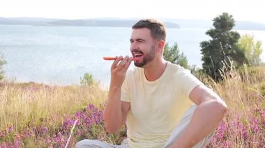 Sahada oturan mutlu adam akıllı telefon kullanıyor..