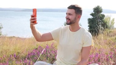 Sahada oturan mutlu adam akıllı telefon kullanıyor..