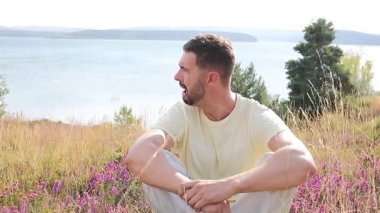 Çiçeklerle dağların tepesinde oturan yakışıklı adam.