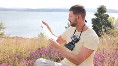 Gölün ve çiçeklerin arka planında kamerası olan yakışıklı bir fotoğrafçı.