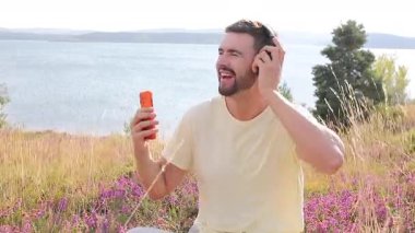 Neşeli Adam Kablolu Kulaklıkla Müzik Dinliyor ve Açık havada Göl kenarında Smartphone
