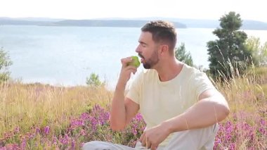 Mutlu genç adam doğada elma yiyor.