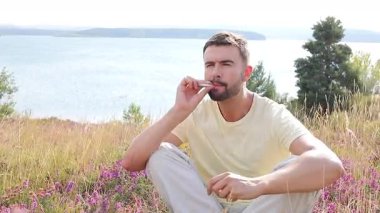 Genç adam, gölün kenarında elinde çiçeklerle sigara içiyor.