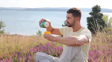 Termoslu genç bir adam Çiçekli çayır ve göllü bir çay