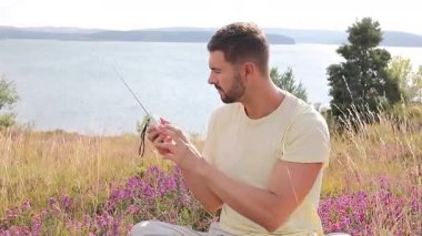 Bir adam bir göl kenarındaki yamaçta oturuyor, elinde radyo var.