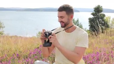 Gölün ve çiçeklerin arka planında kamerası olan yakışıklı bir fotoğrafçı.