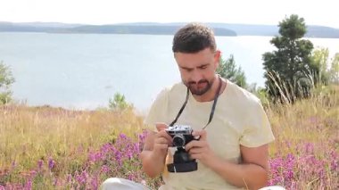 Gölün ve çiçeklerin arka planında kamerası olan yakışıklı bir fotoğrafçı.