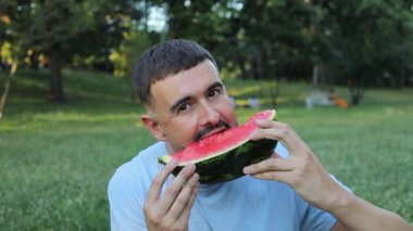 Yeşil çimlerde karpuz yiyen yakışıklı adam.