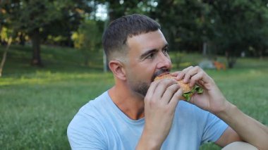  Yakışıklı adam parkta hamburger yiyor..