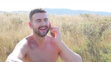 Sahada oturan mutlu adam akıllı telefon kullanıyor..