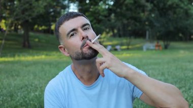 Genç adam parkta sigara içiyor.