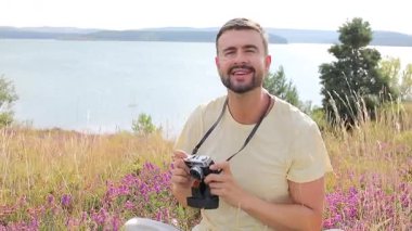 Gölün ve çiçeklerin arka planında kamerası olan yakışıklı bir fotoğrafçı.