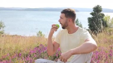 Mutlu genç adam doğada elma yiyor.