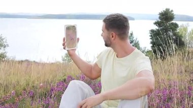 Gölün ve çiçeklerin arka planında ayna olan genç bir adam.