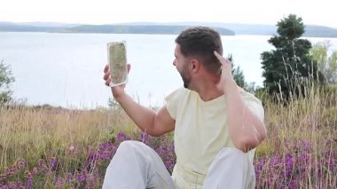 Gölün ve çiçeklerin arka planında ayna olan genç bir adam.