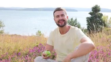 Mutlu genç adam doğada elma yiyor.