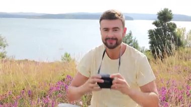 Gölün ve çiçeklerin arka planında kamerası olan yakışıklı bir fotoğrafçı.