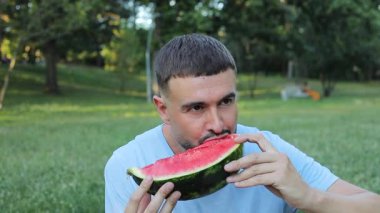 Yeşil çimlerde karpuz yiyen yakışıklı adam.
