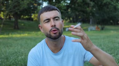Genç adam parkta sigara içiyor.
